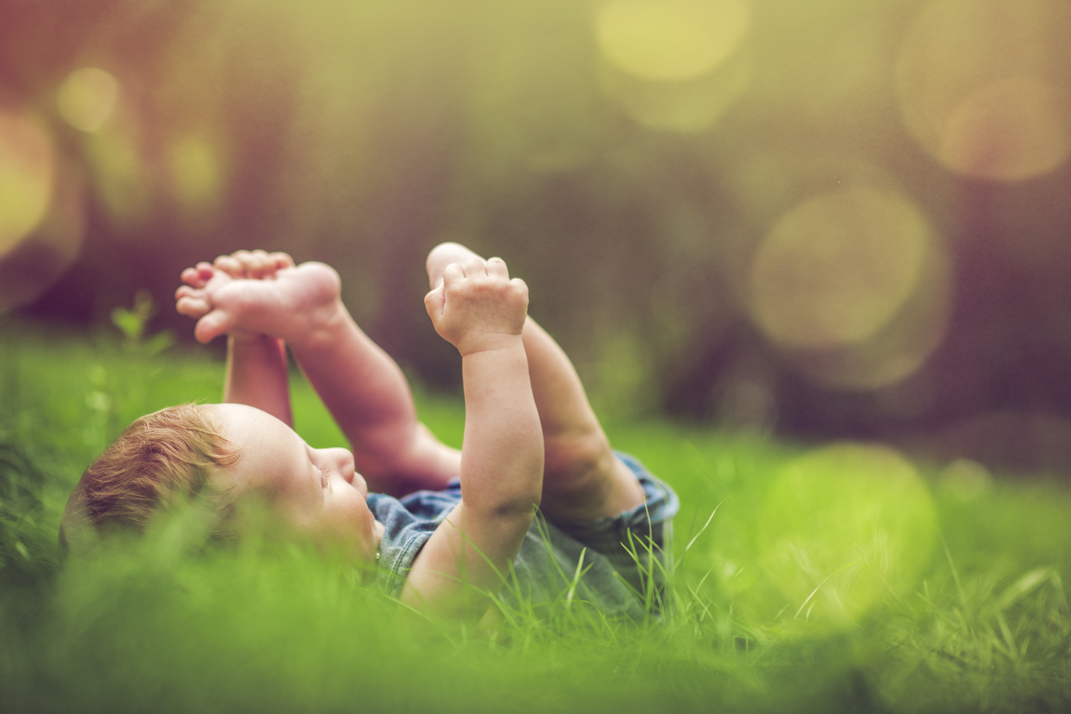 Cute baby playing with his legs on the grass