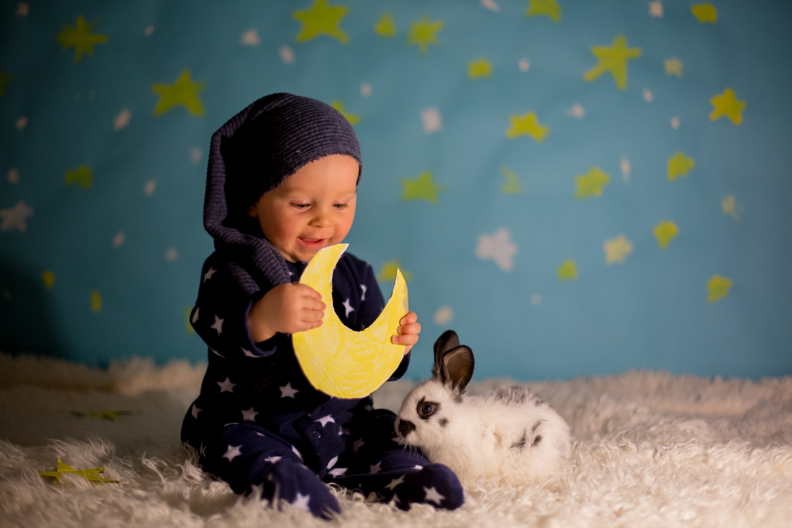 Little child, baby boy with cute white bunny and moon on a blue star and moon background