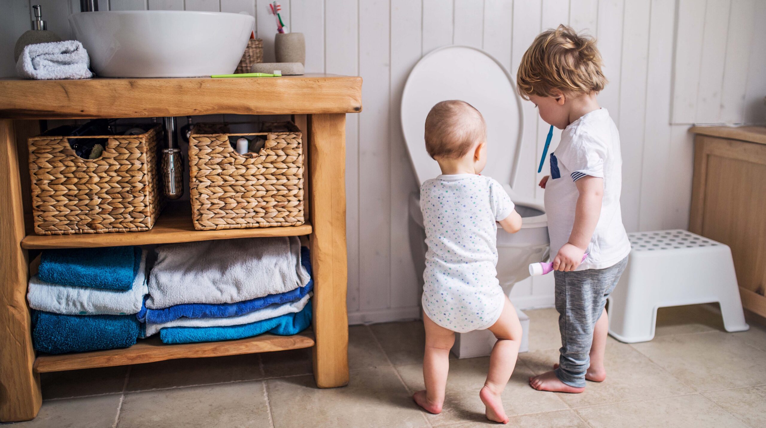 Two toddler children with toothbrush standing by the toilet in the bathroom at home.