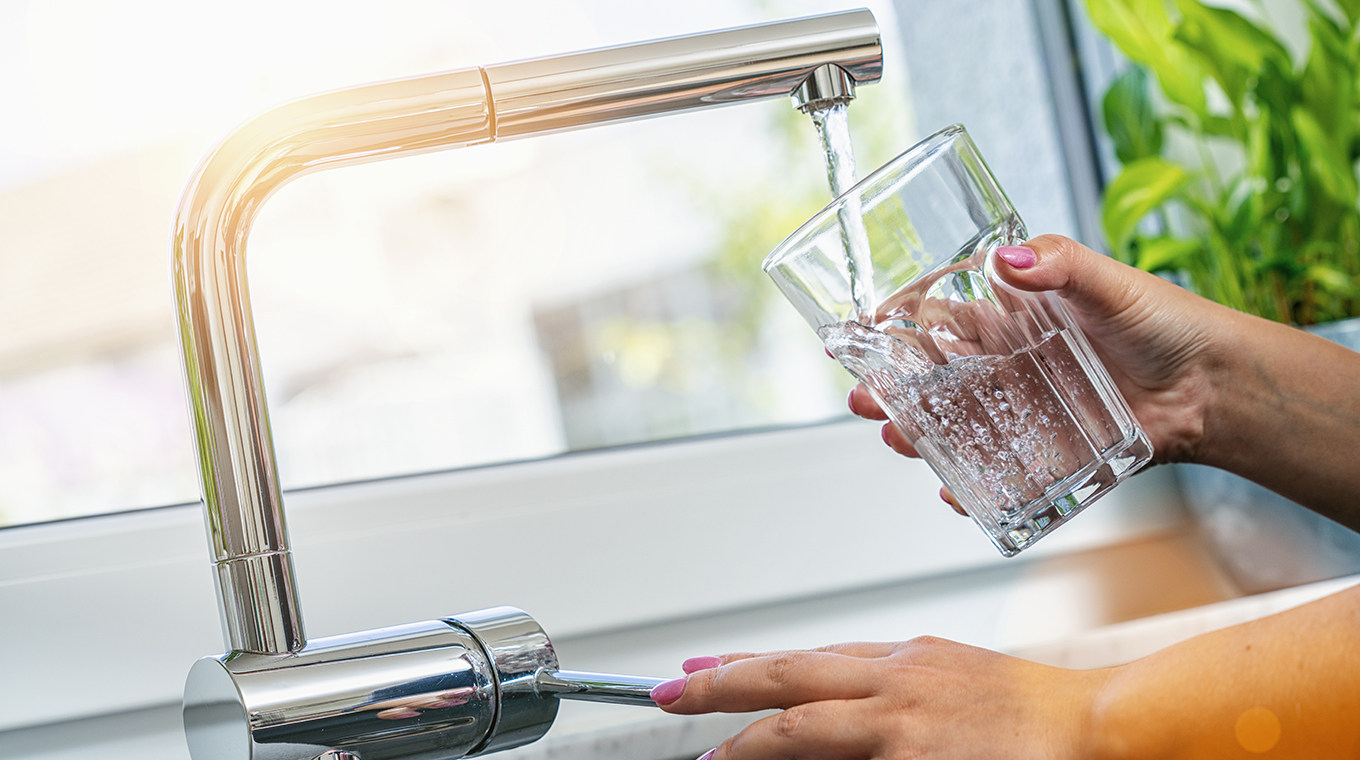 woman holding glass at water tap and filling water