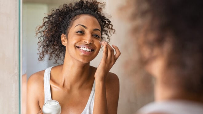 woman moisturizing face in mirror