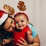 Mom kissing her baby wearing reindeer antlers