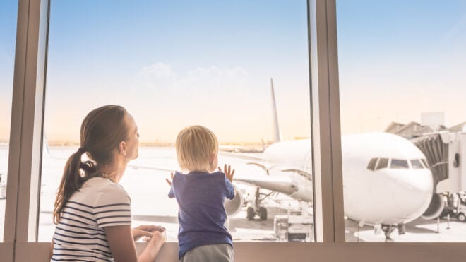 Mother and son at airport boarding terminal looking out window at airplane. Family travel and adventure.