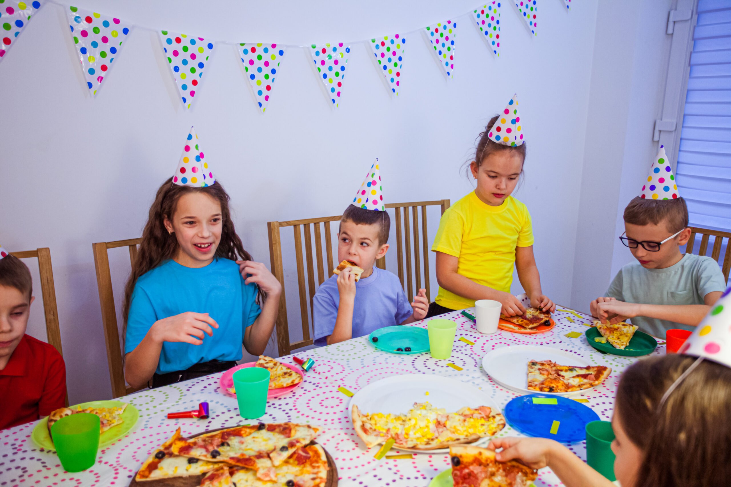 The group of little friends eating at the birthday party. The kids are eating pizza and talking
