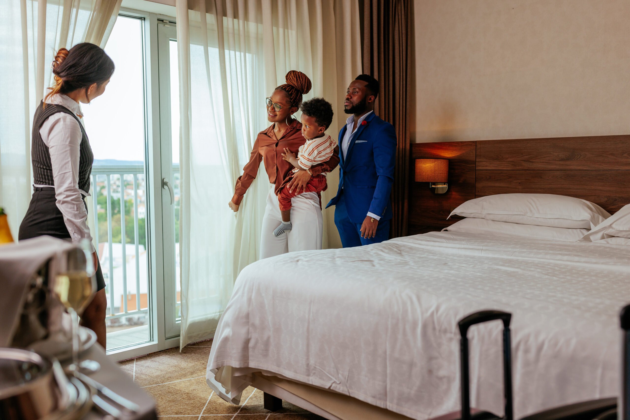 A wealthy African American family is in a luxurious hotel with the concierge showing them around the apartment and enjoying the view from the window.