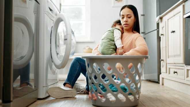Mother, baby and basket in kitchen for laundry, housekeeping and motherhood in house with sleeping child. Woman, newborn and tired with washing machine for cleaning clothes, parenthood and burnout