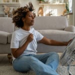 Young African American woman cooling down by ventilator at home, feeling unwell during heatwave