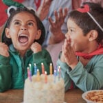 Happy birthday, party and children in halloween costume to celebrate young and fun girls special day together. Cake, fantasy and excited kid in a dinosaur monster outfit and boy in a superheroes cape