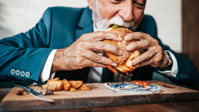 Handsome senior business man sitting in restaurant and enjoying in delicious burger. People and food concept.