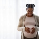 Smiling young black pregnant woman holding hands on big belly