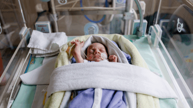A baby with their arms stretched over their head while in a cot in the NICU