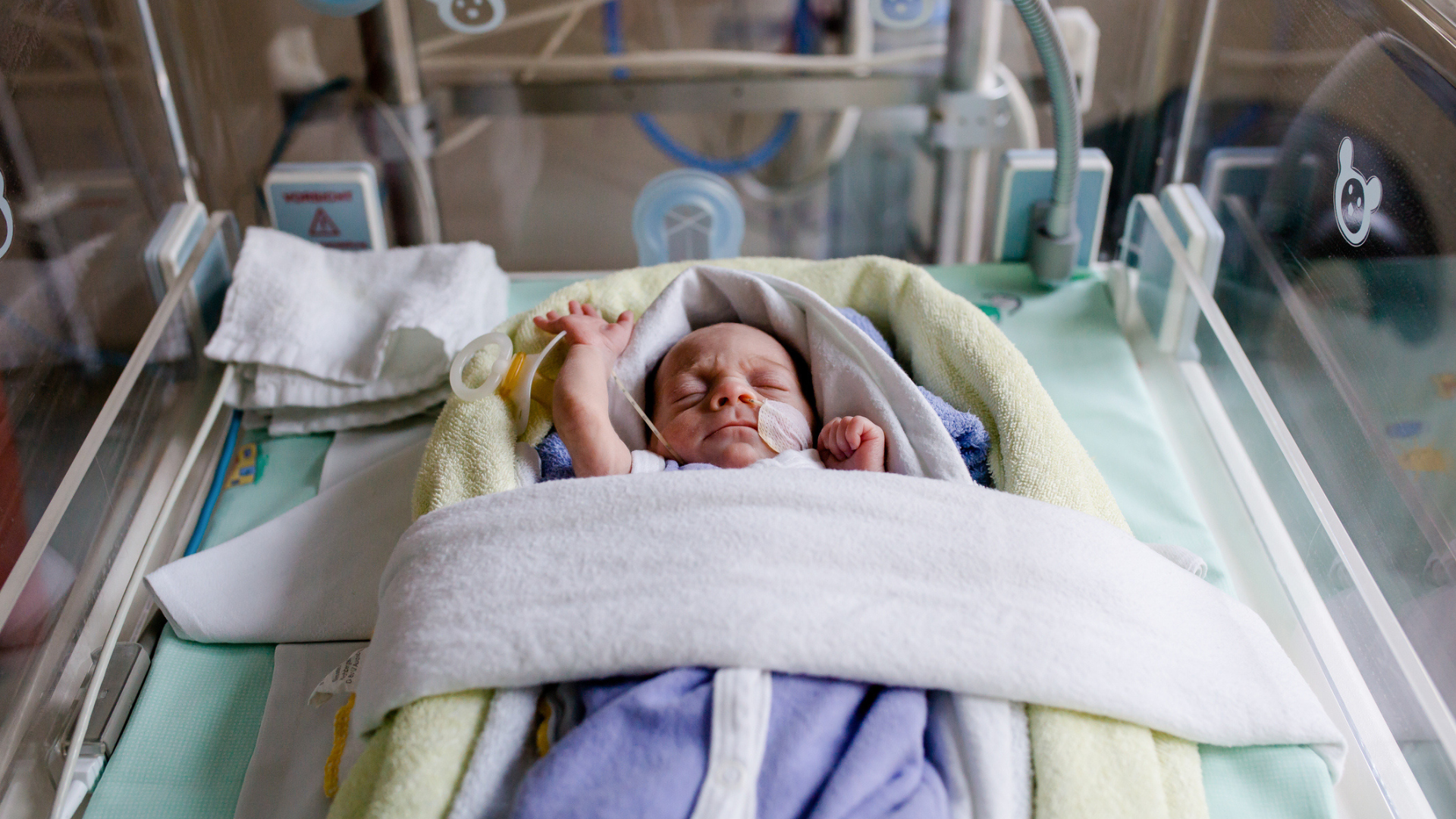 A baby with their arms stretched over their head while in a cot in the NICU