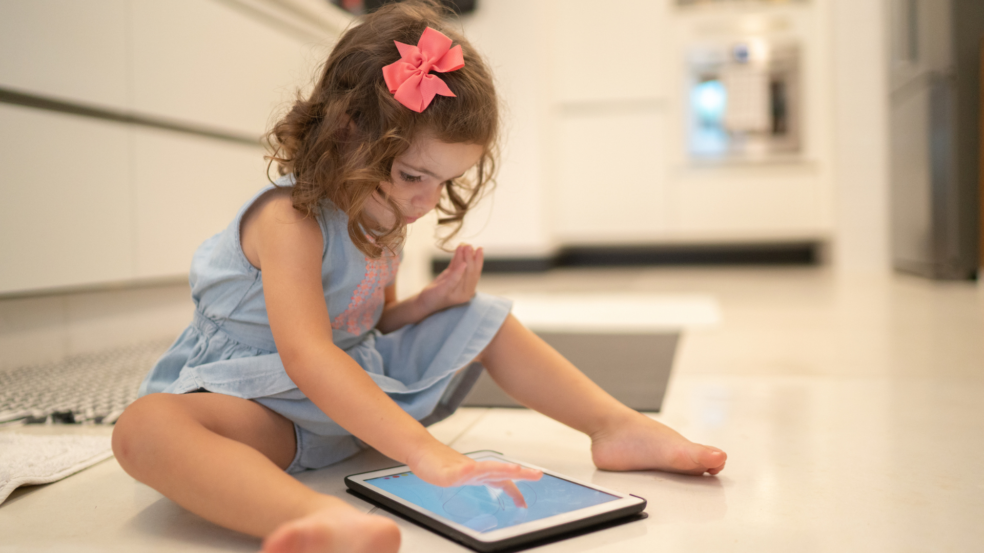little girl playing on an ipad sitting on the kitchen floor