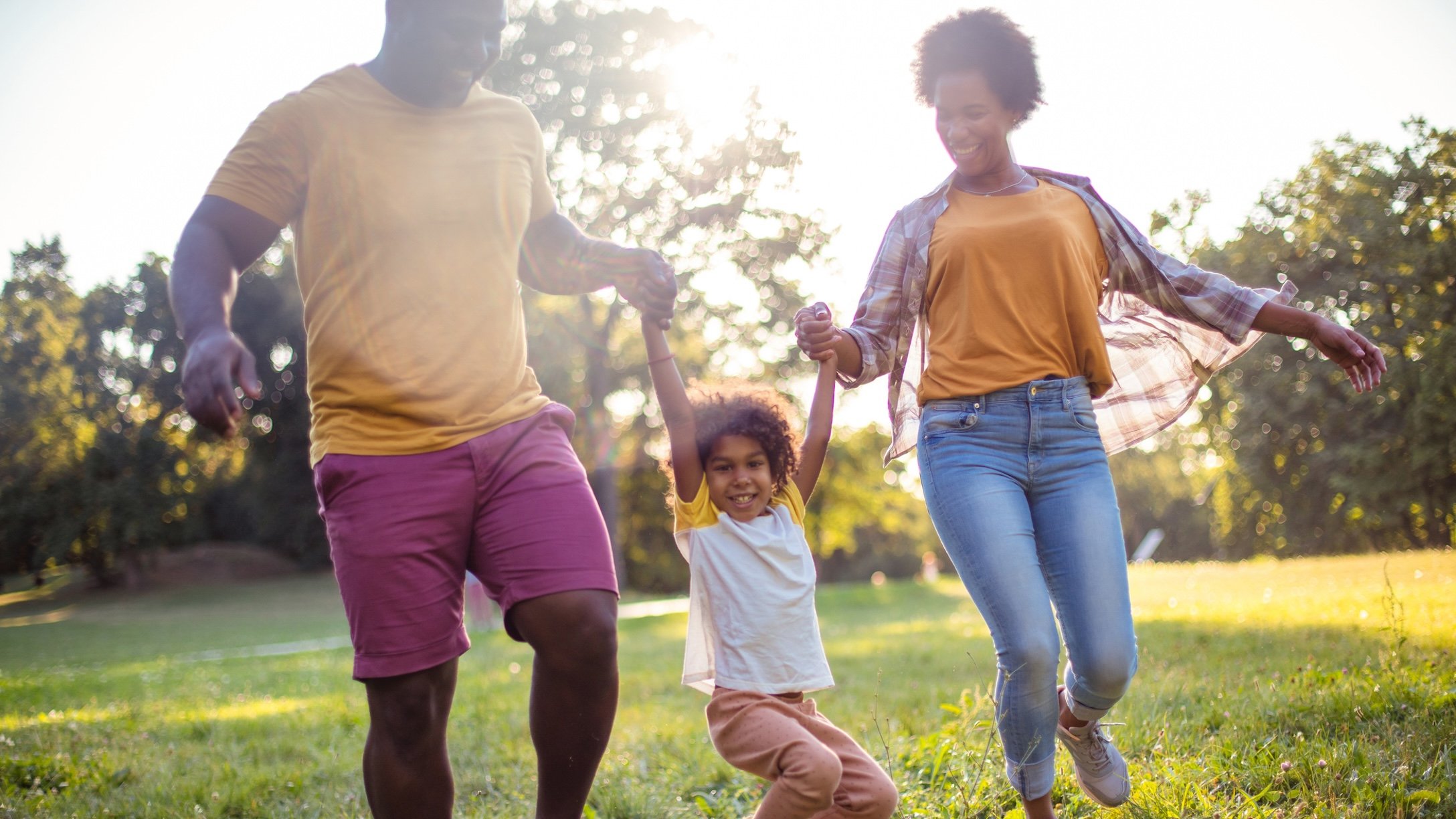 two Black parents playing with daughter outside