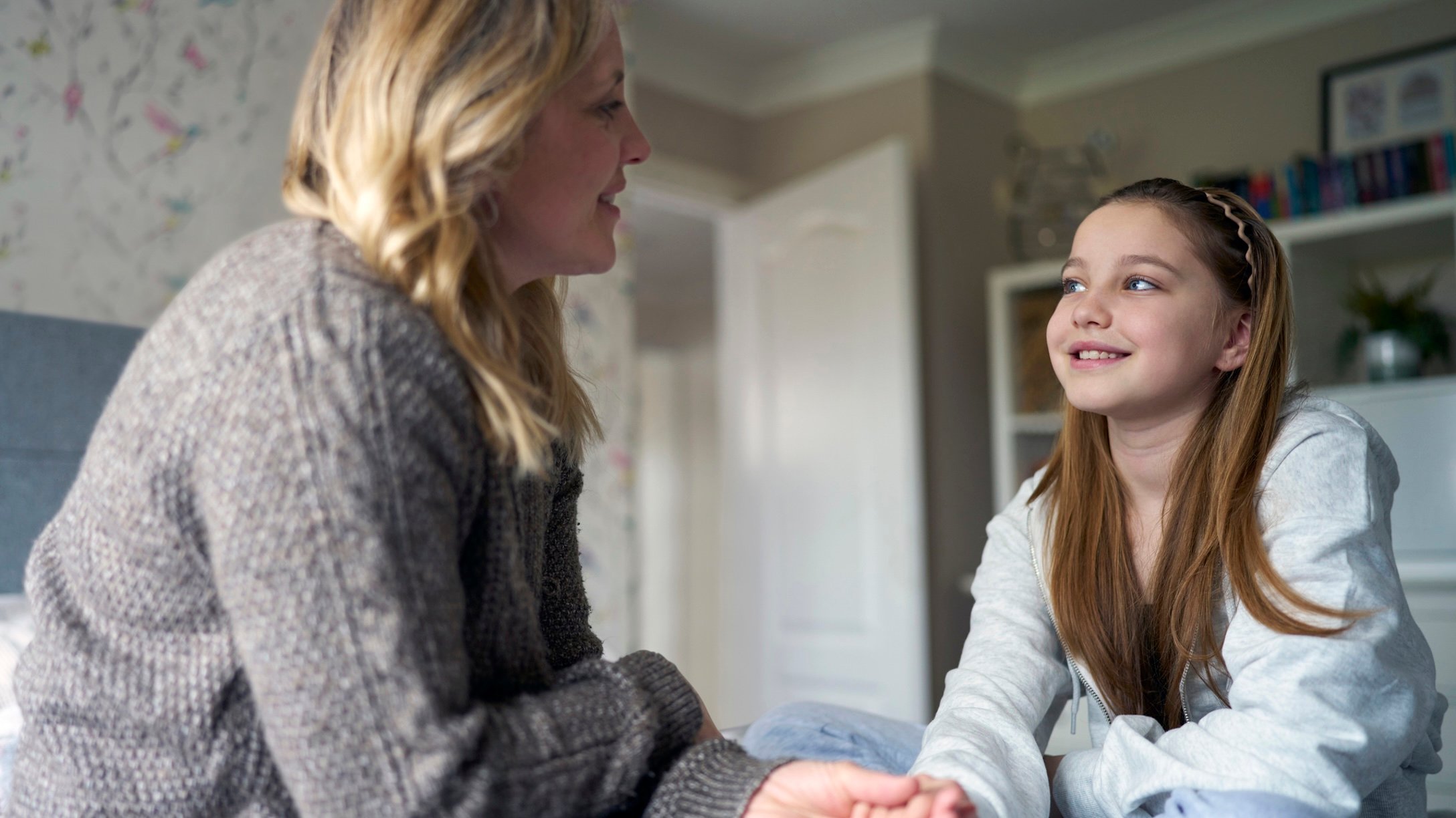 Mom and tween daughter sitting on bed talking
