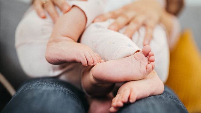Closeup of mom's hands holding two baby girls on her lap.
