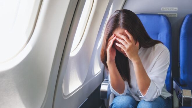 An upset woman on an airplane covering her face as she sits in her seat