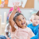 little girl raising hand in classroom