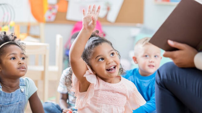 Preschool age girl raises her hand to ask or answer a question in her classroom