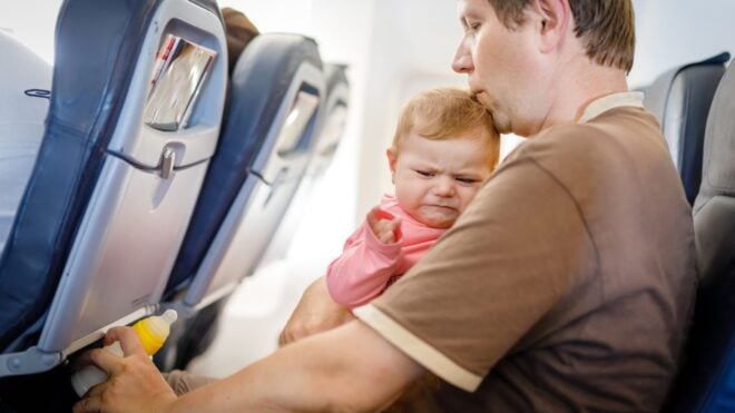 A dad trying to comfort his crying baby while on a flight with a bottle in his hand