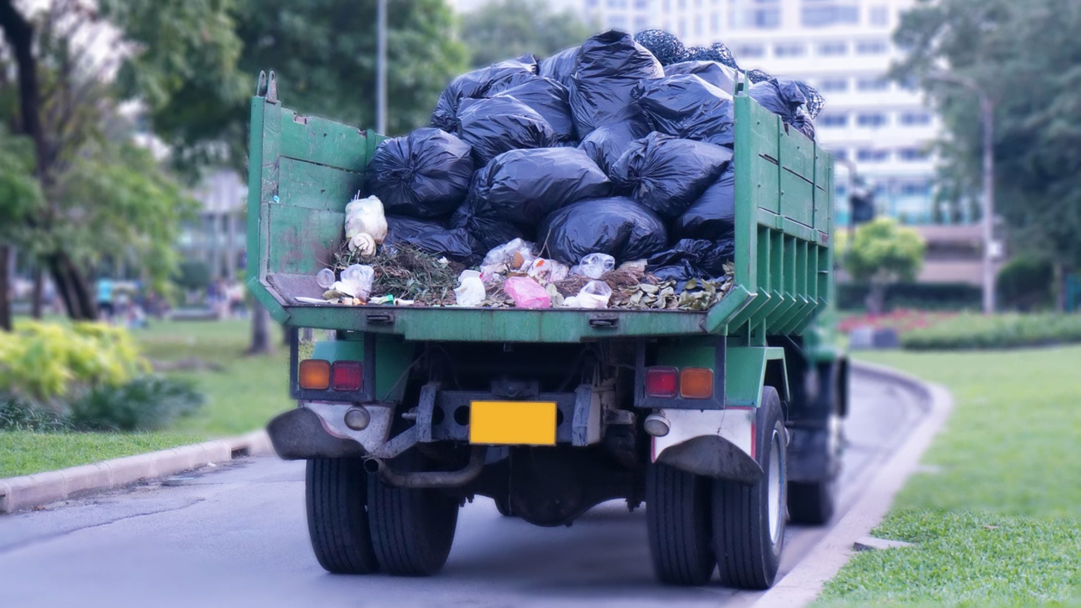 A garbage truck on the street filled with trash and trash bags