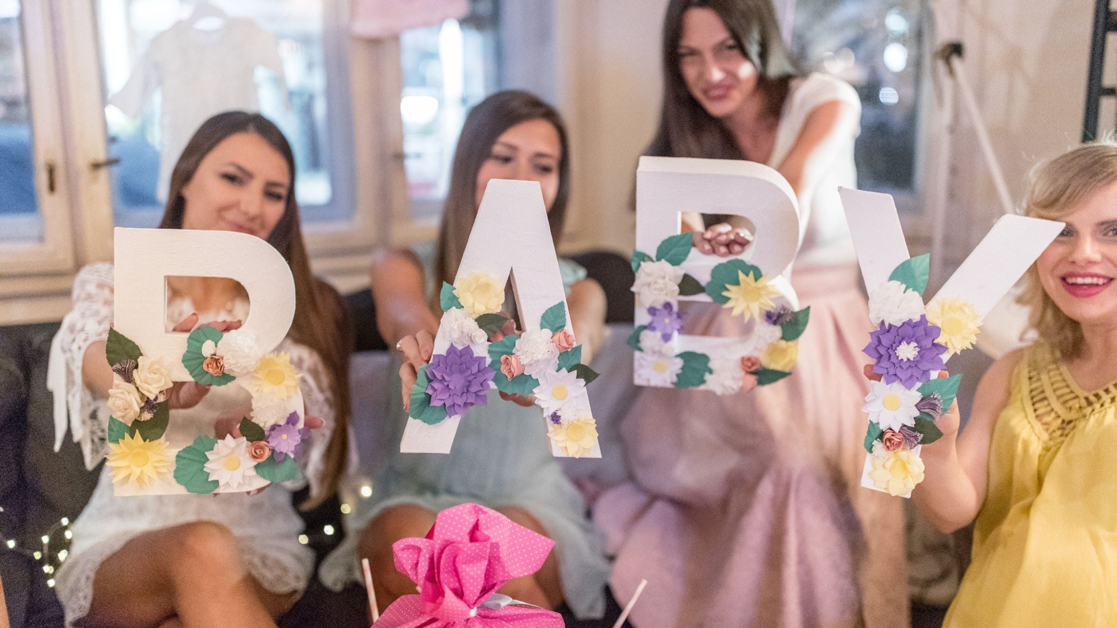 A photo of four women each holding up a decorative letter that spells out BABY