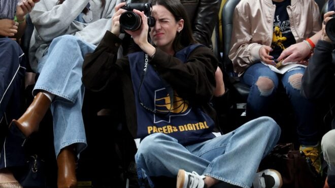 Caitlin Clark of the Indiana Fever sits on the baseline and makes photographs during the Indiana Pacers game