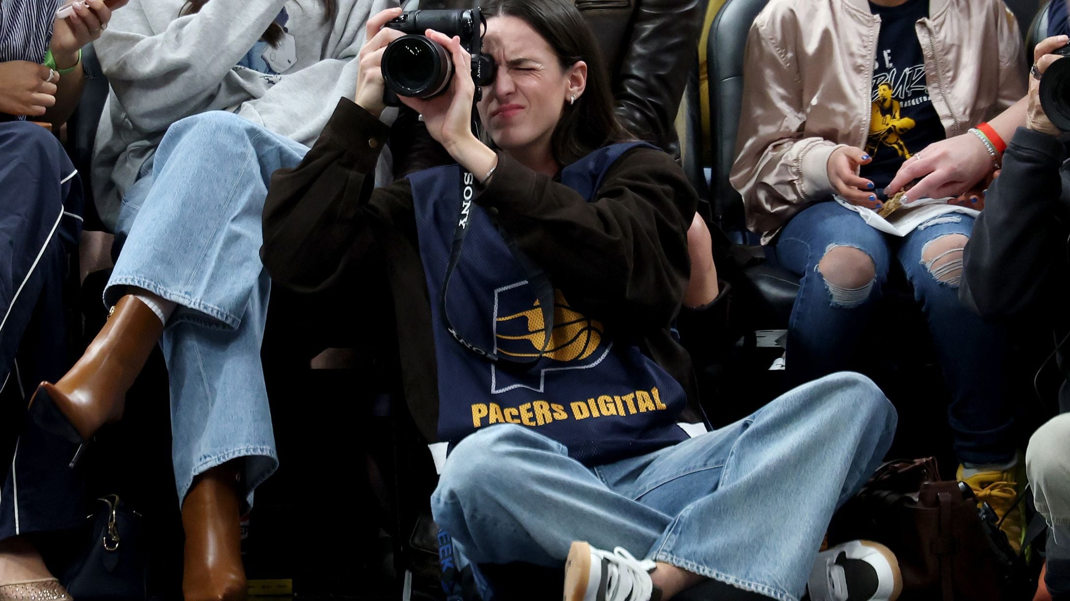 Caitlin Clark of the Indiana Fever sits on the baseline and makes photographs during the Indiana Pacers game
