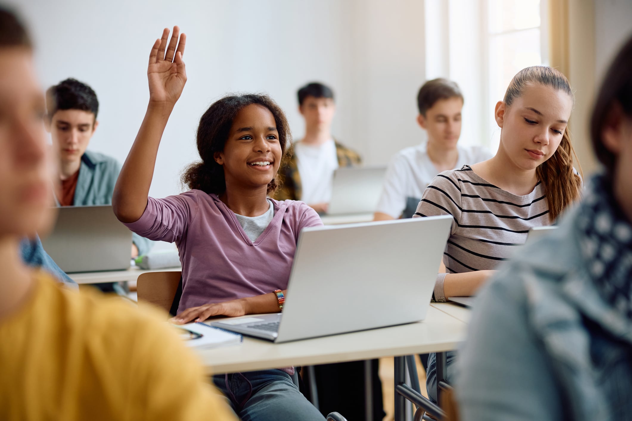 Happy black high school student raising her arm during computer class in the classroom.