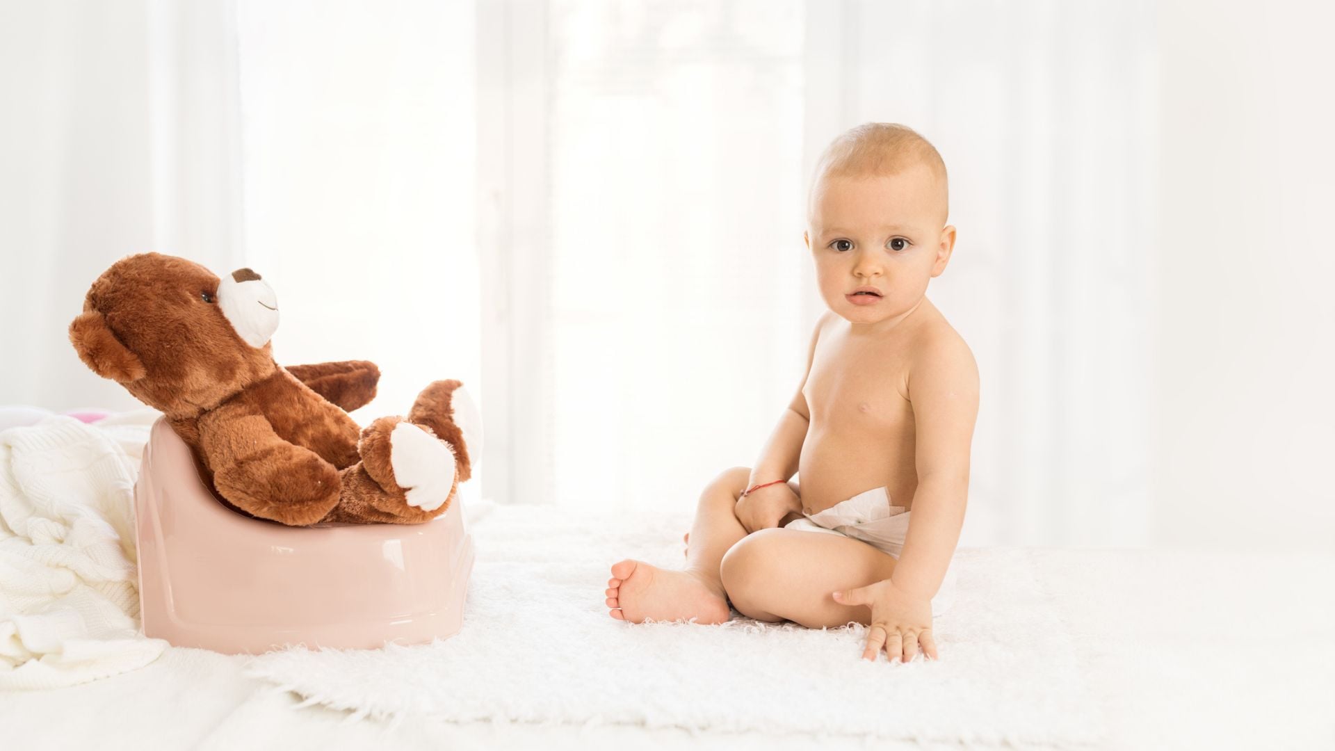 A baby in a diaper with their teddy bear across from them on a potty
