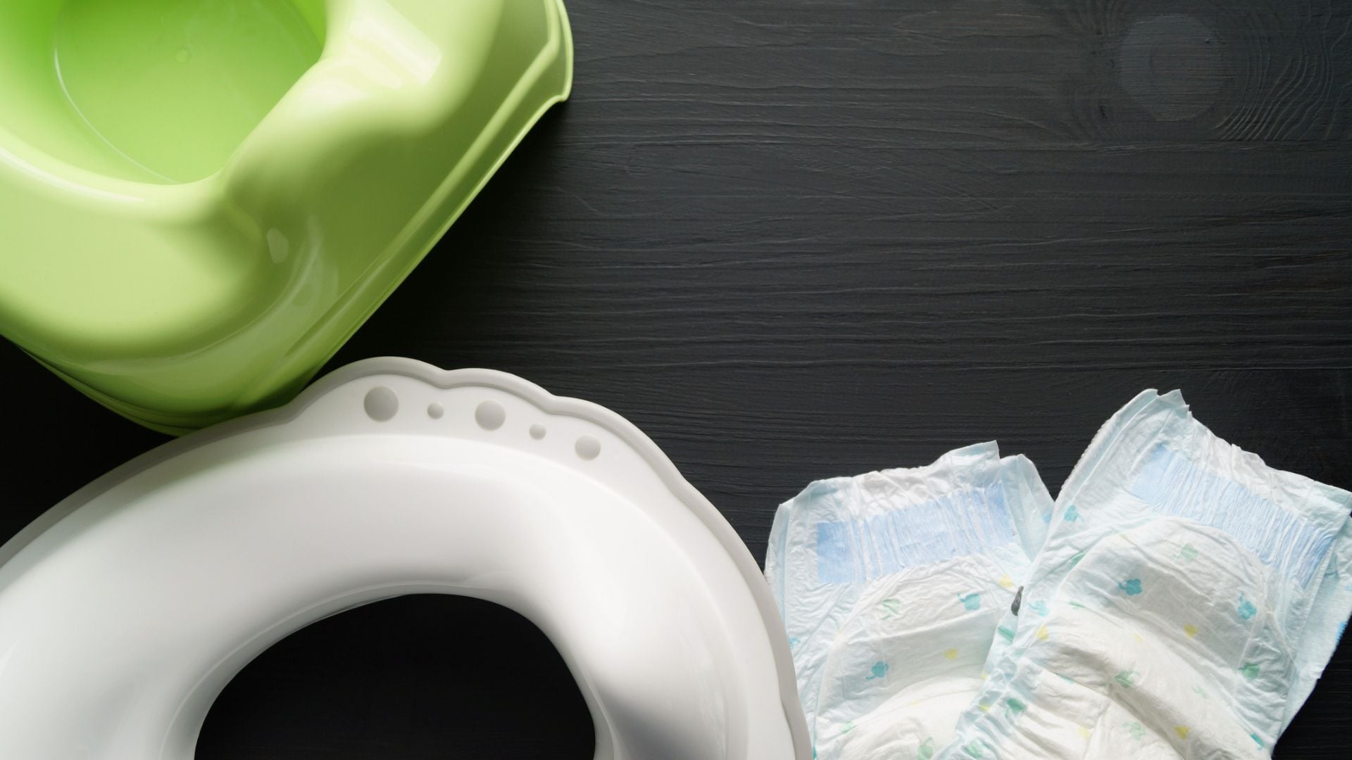 A green potty, a potty for the toilet, and two diapers on the floor