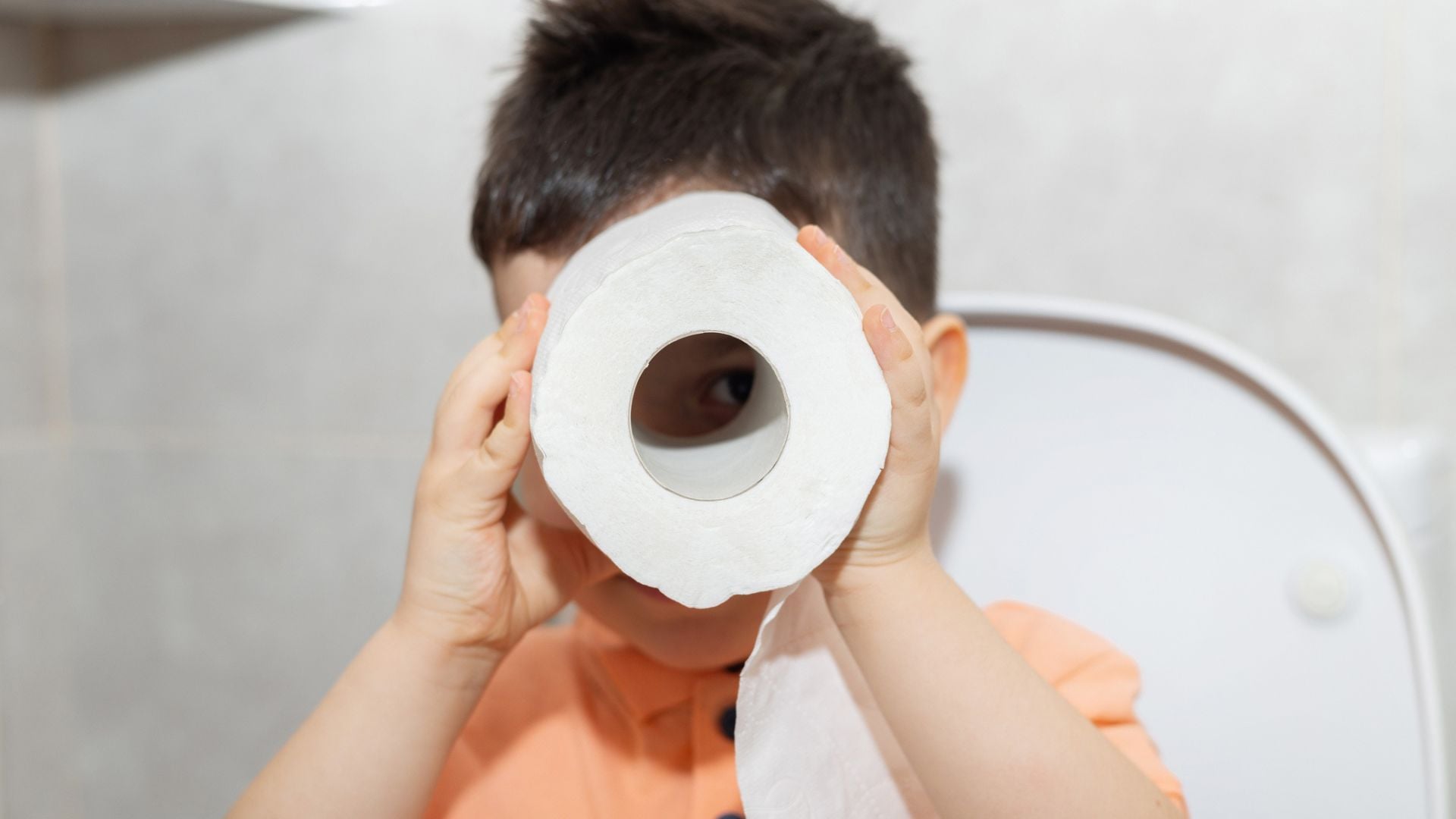 A little boy staring through a roll of toilet paper he's holding up