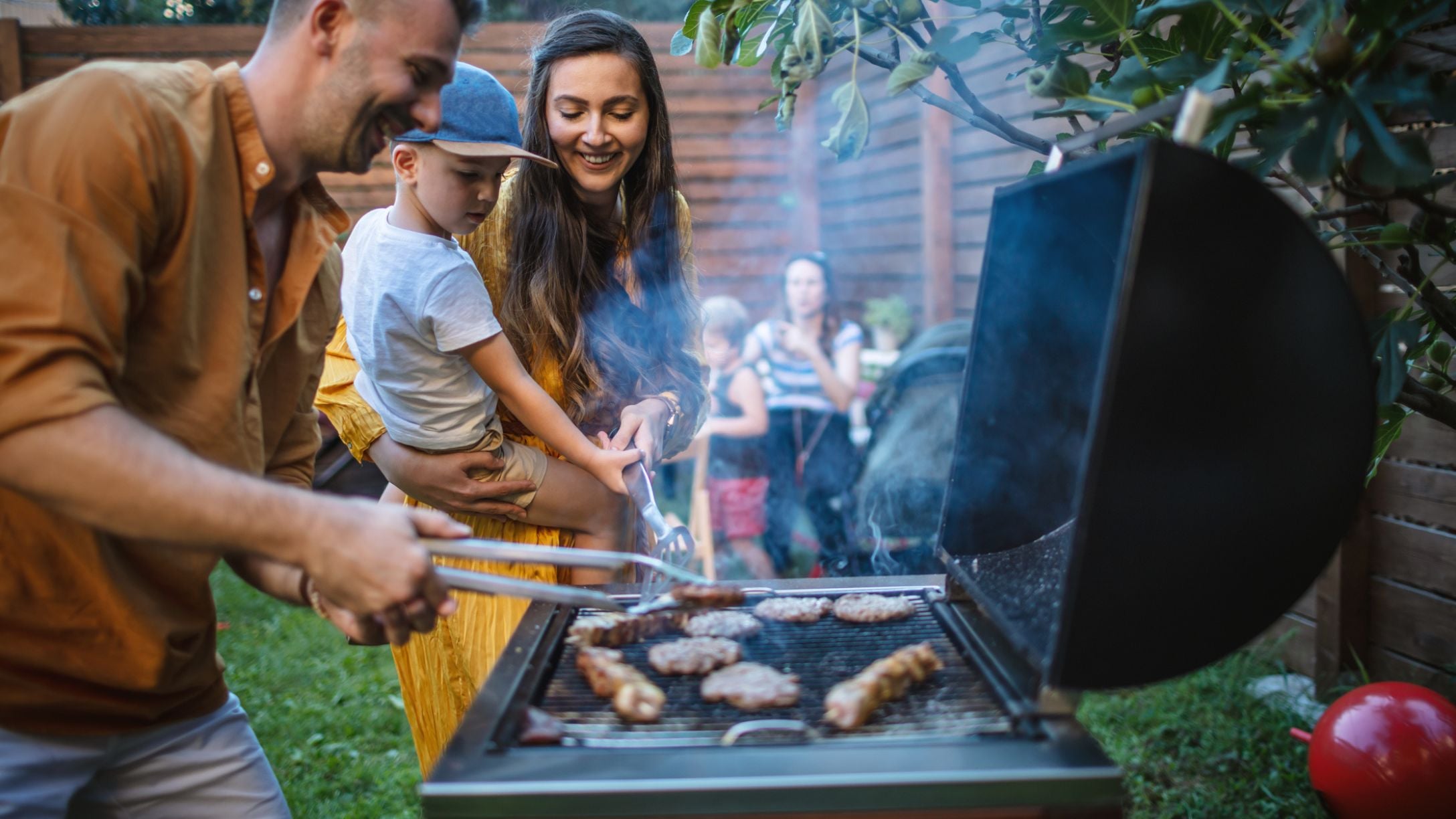 A man barbecuing with a woman and her child nearby