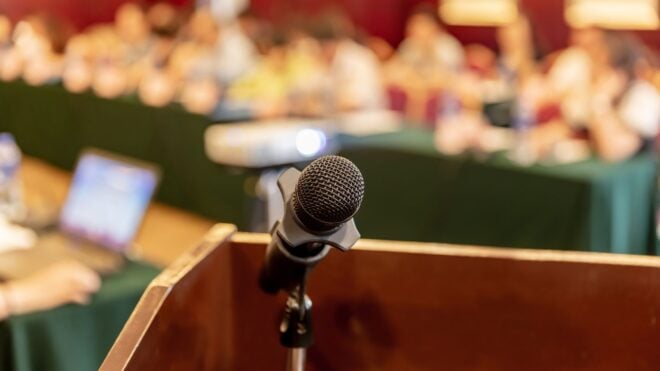 A microphone in a conference room with blurred people in the background
