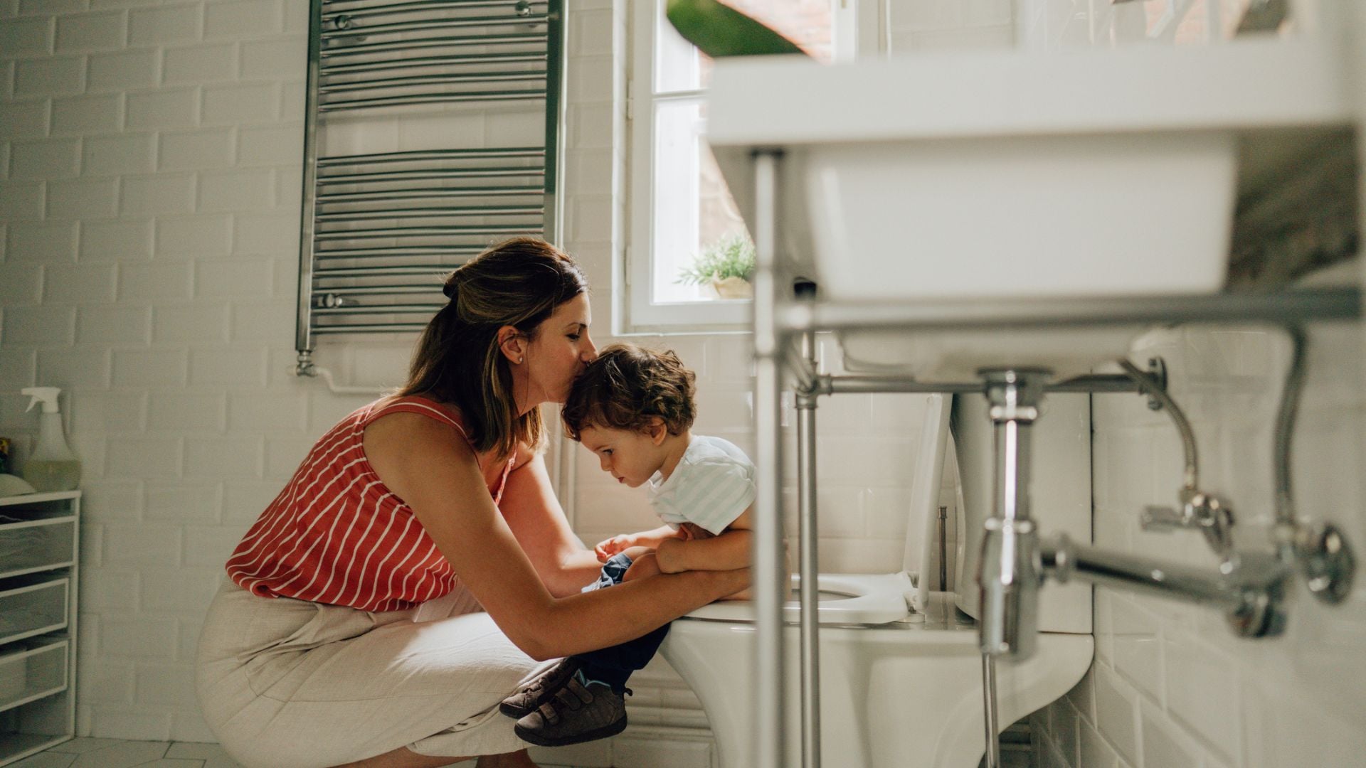 A mom kissing her little boy's forehead while he's sitting on the potty