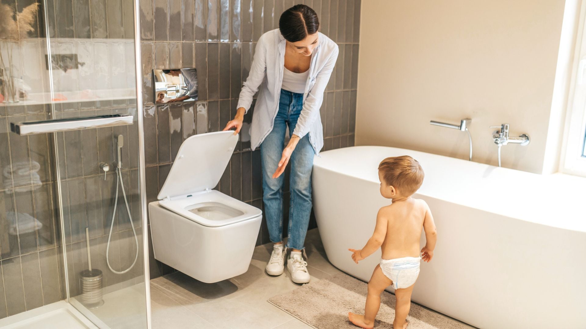 A mom showing her diapered toddler the toilet in a modern bathroom