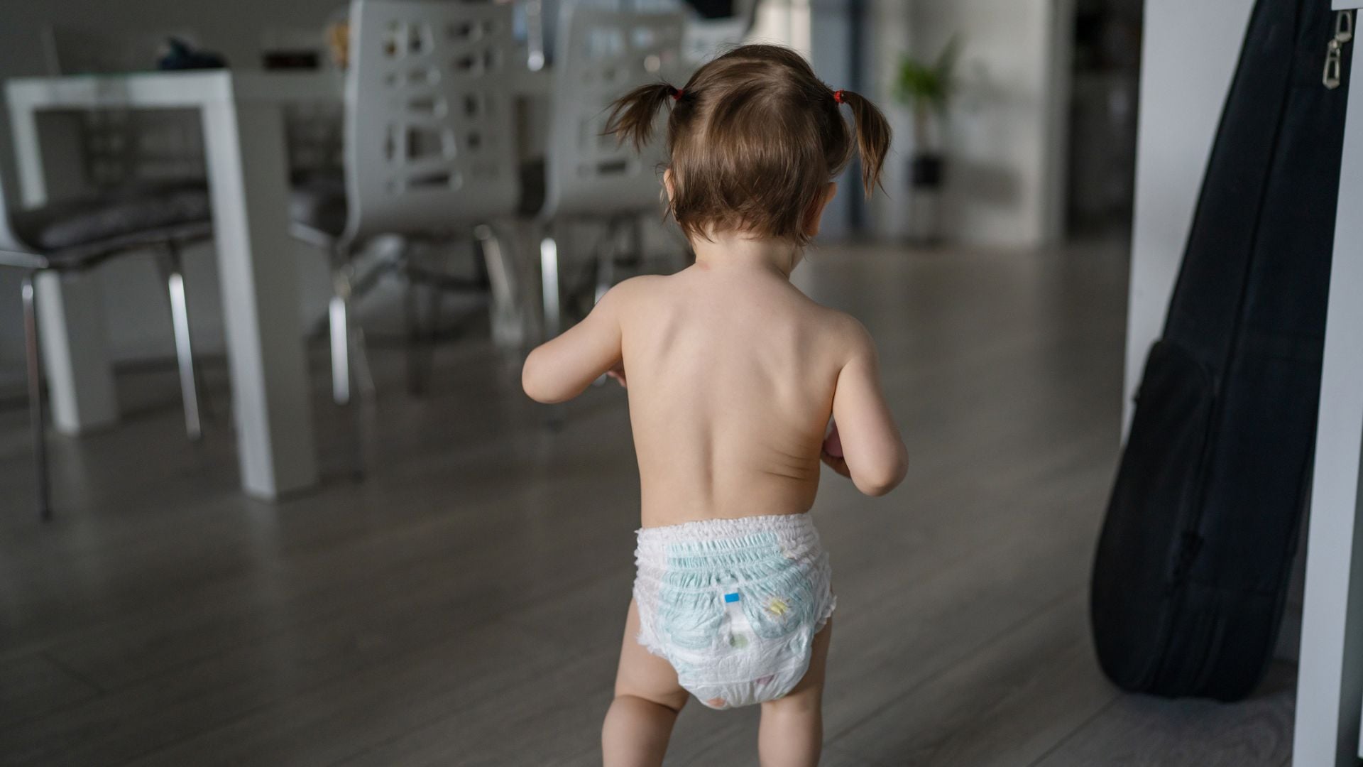 A toddler in pigtails wearing a pull-up walking through a kitchen