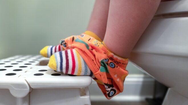 A toddler with colorful socks and underpants with their feet on a stool while sitting on a toilet