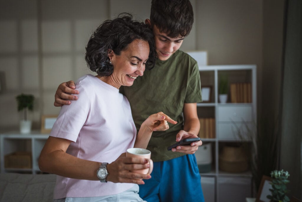 mother and teenage son use mobile phone together in modern living room