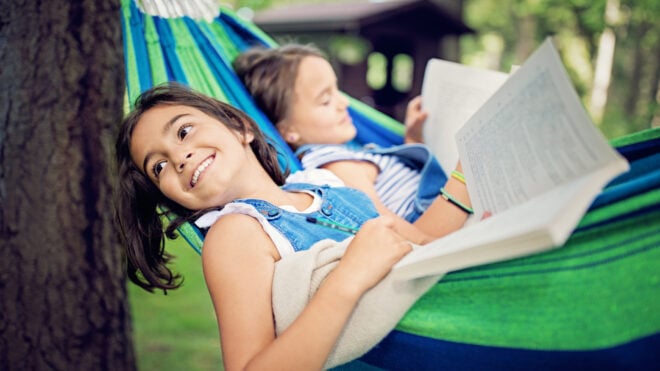 Two girls are lying down in the hammock and reading books